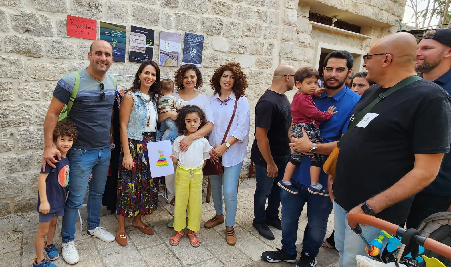 משפחות עם ילדים מצטלמות ליד קיר אבן שעליו כרזות