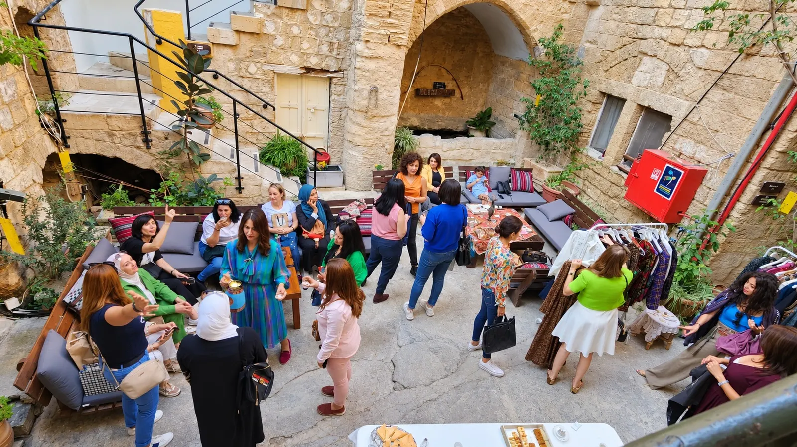 נשים מתכנסות בחצר אבן עתיקה, יושבות על ספסלים ומעיינות בבגדים על מתלים