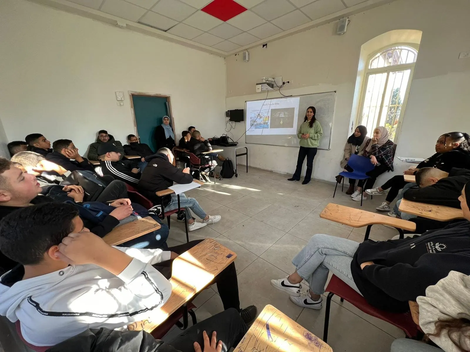 הרצאה בכיתה: תלמידים יושבים ומקשיבים למרצה ליד לוח