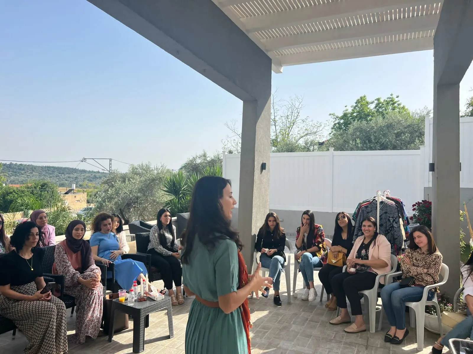 אישה בשמלה ירוקה מדברת מול נשים היושבות במרפסת פתוחה
